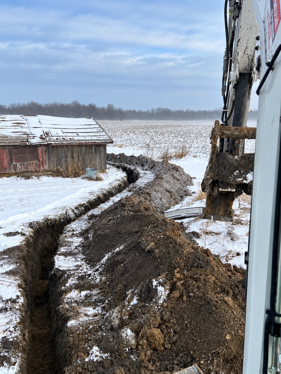 Utility trench excavation through a snow-covered farm field